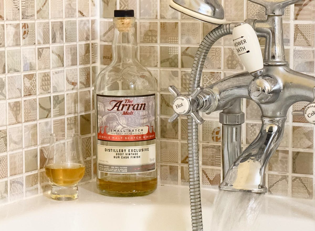 A photo of a bottle of whisky sat on the side of a bath with a glass next to it.