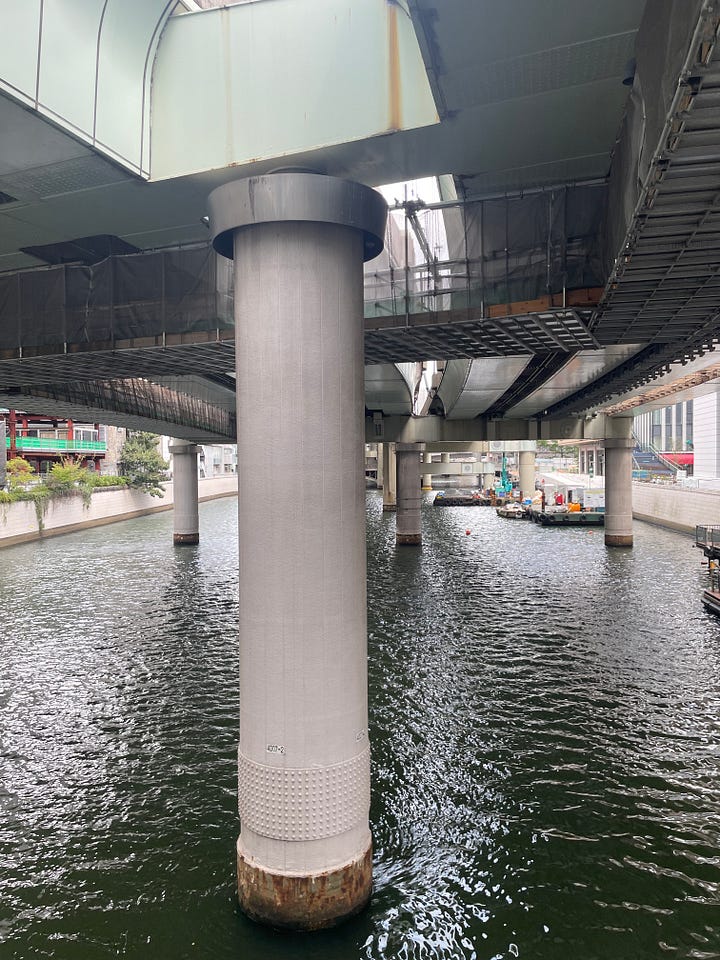 Four photographs of the bridge and the river beneath it, all of which are dominated by the expressway viaducts, which stand on thick concrete pillars dropped haphazardly into the river and fill almost its complete width, putting the bridge and river entirely into shade and blocking much of the sky.