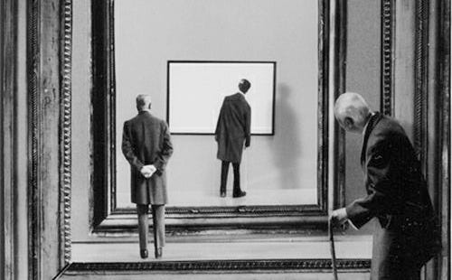 This may contain: black and white photograph of two men looking at an art work