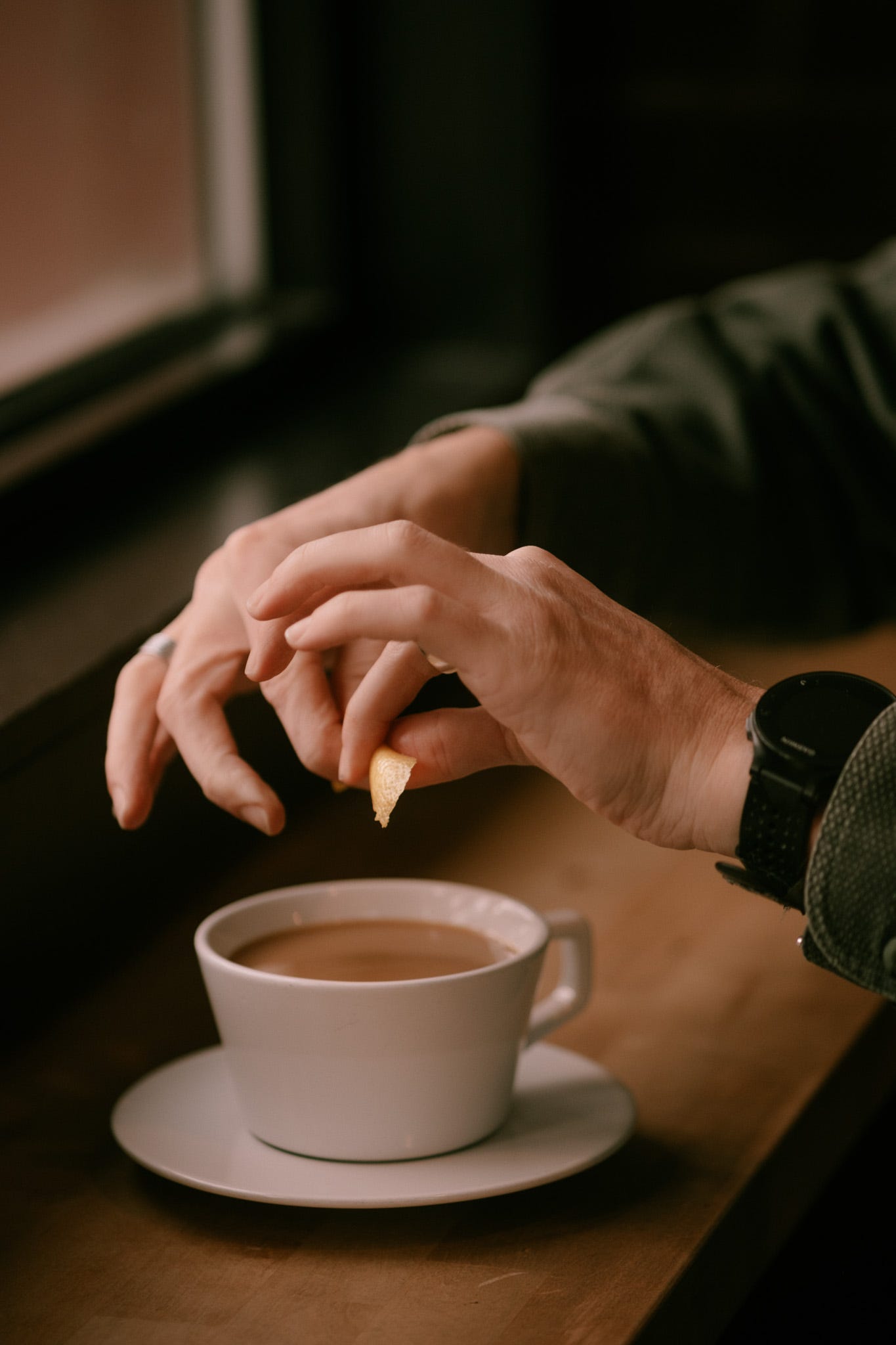 Close-up of two hands expressing a lemon peel into a cup of tea