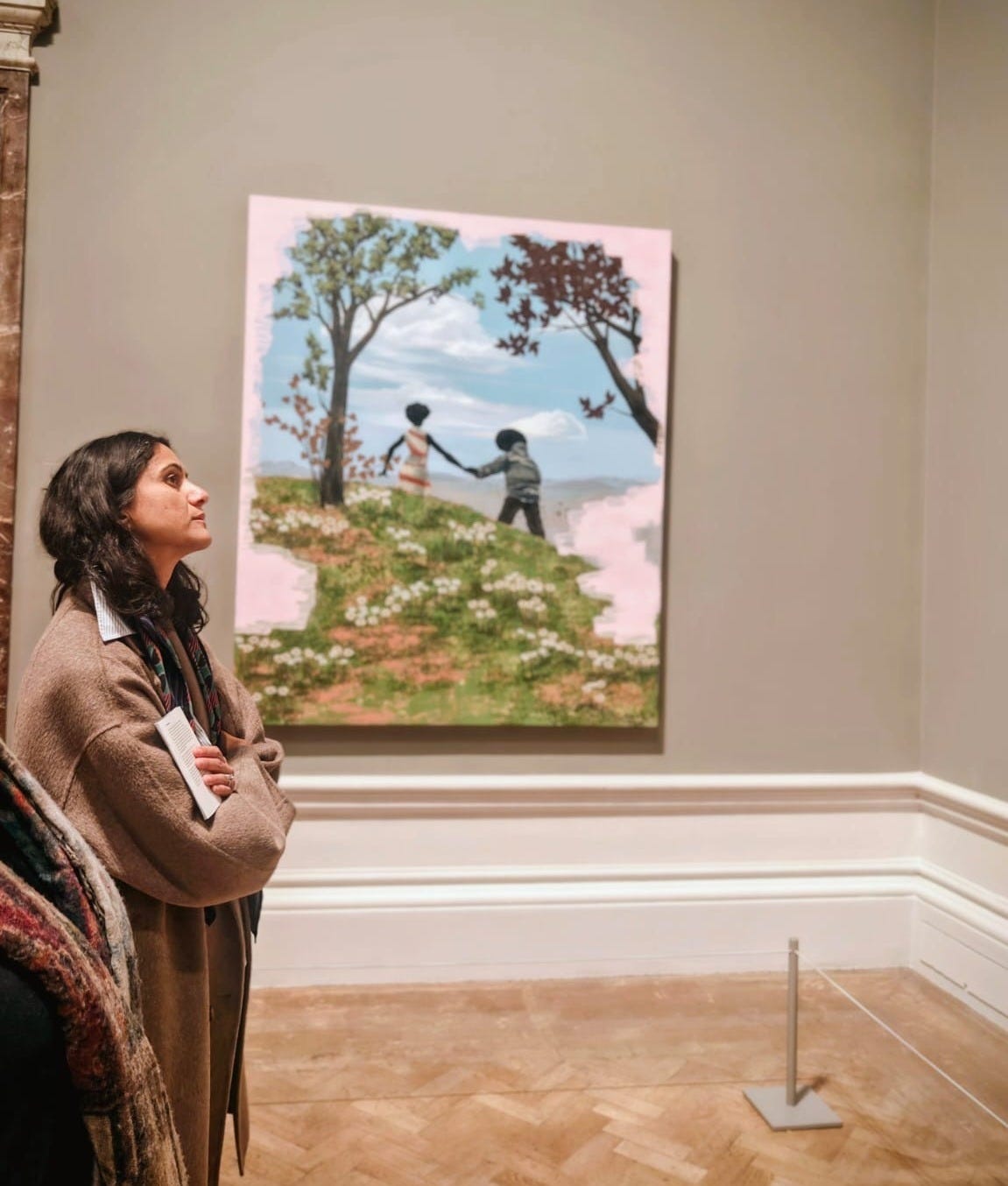 Anar stands in a gallery, looking up at a Kerry James Marshall painting in a gold frame.