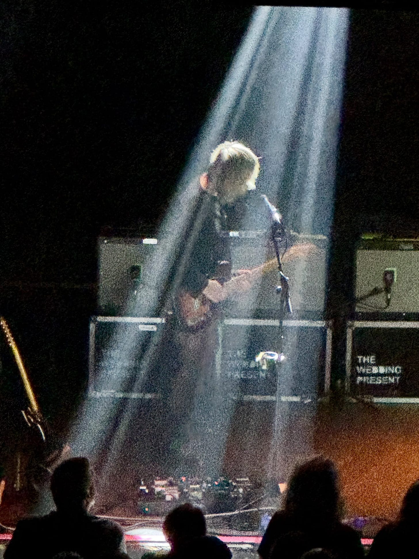 A guitarist under a spotlight on stage, with The Wedding Present amps behind