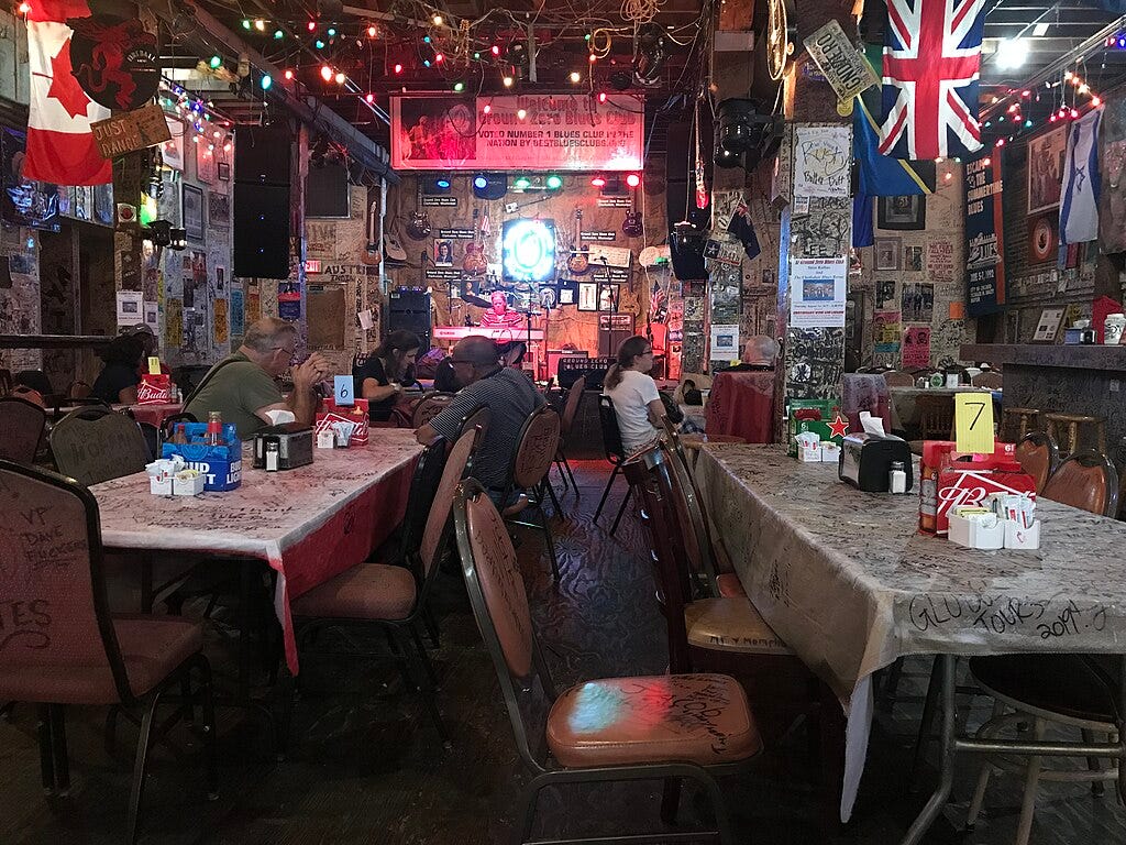 Inside of a club, with tables at the front and a stage in back. Inside of a club, with tables at the front and a stage in back.