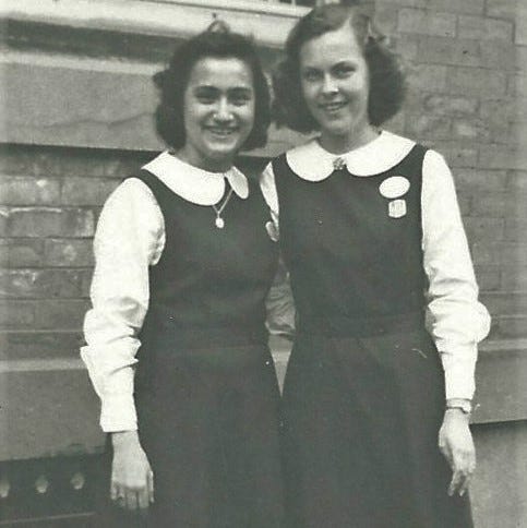 A black and white photo from the 1950s shows two 14-year-old girls in Catholic school jumpers posed on a city street