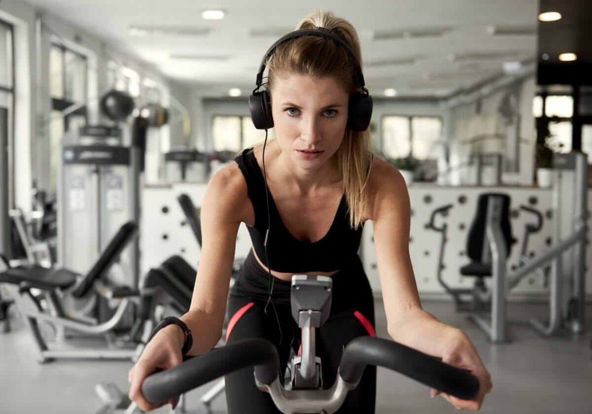 Woman working out on an exercise bike while listening to music Woman working out on an exercise bike while listening to music