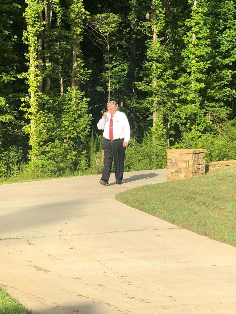 A man dressed in business attire with a shirt and tie walks alone on a sunlit path