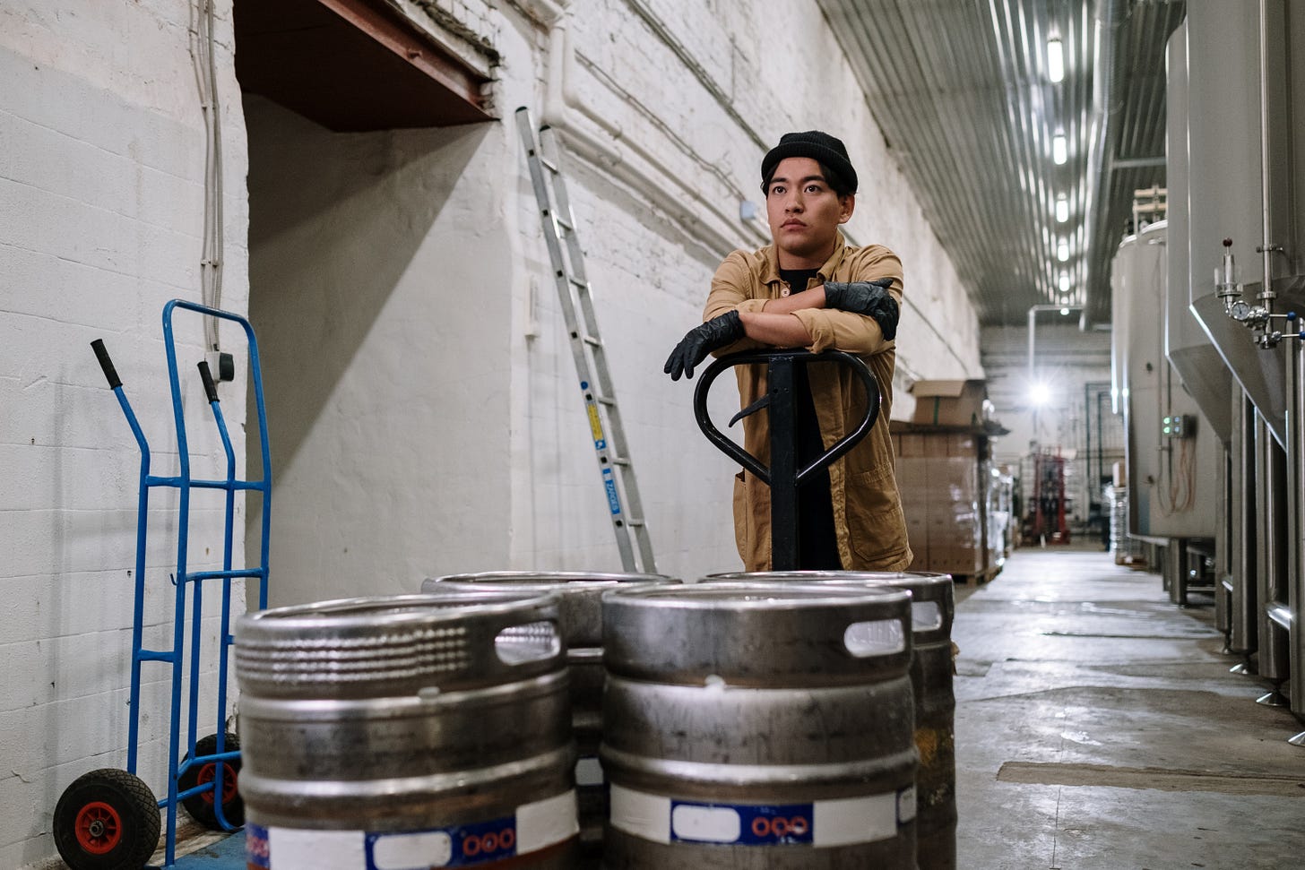 Man looking sad resting his arms on a pallet jack containing kegs of beer Man looking sad resting his arms on a pallet jack containing kegs of beer