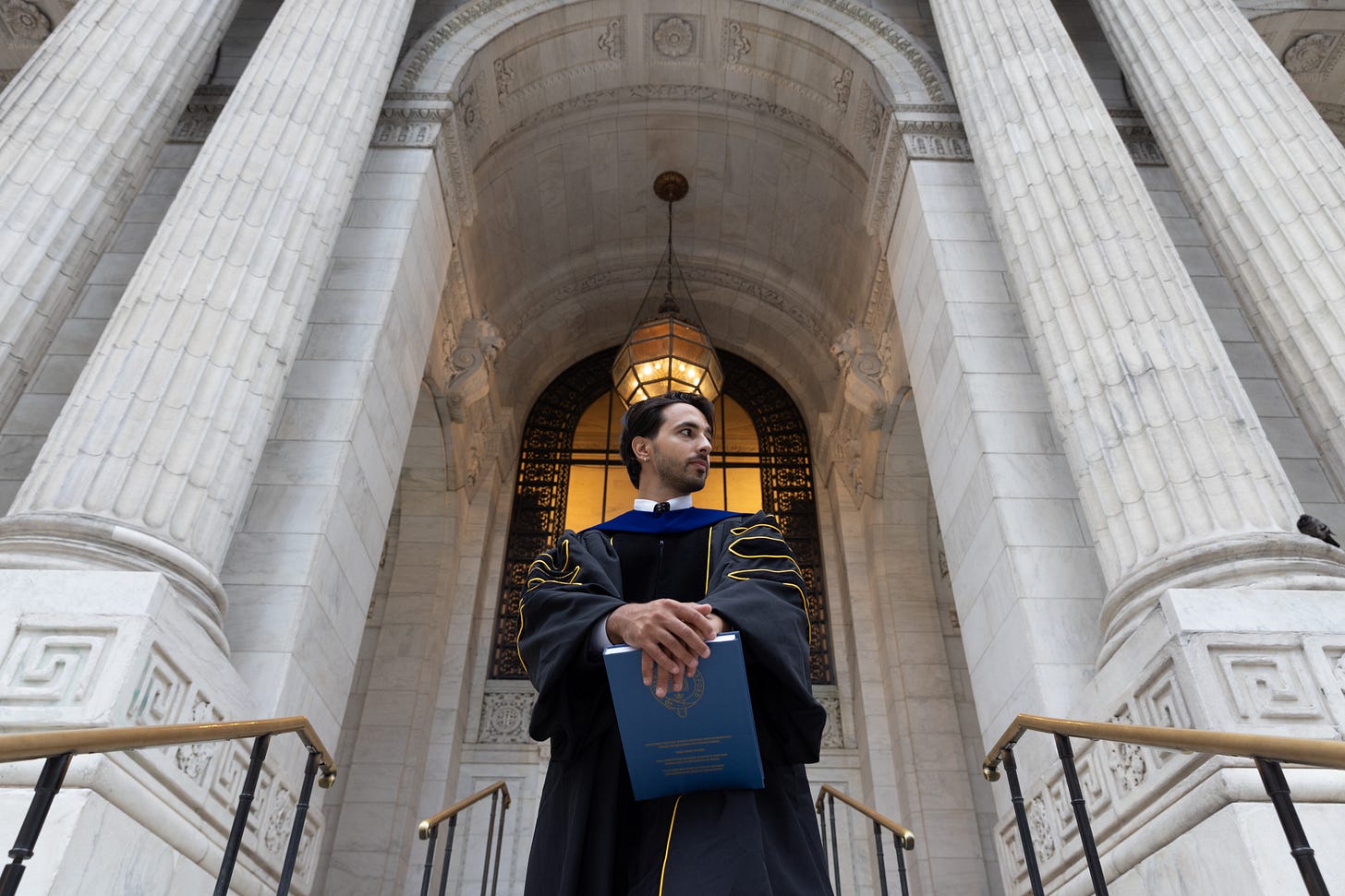 Rayan Semery-Palumbo in doctoral regalia with his dissertation. Rayan Semery-Palumbo in doctoral regalia with his dissertation.