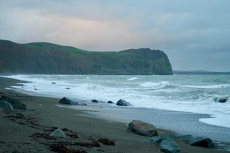 distant green hills sea cliffs and sunset big wave splashing against a rock