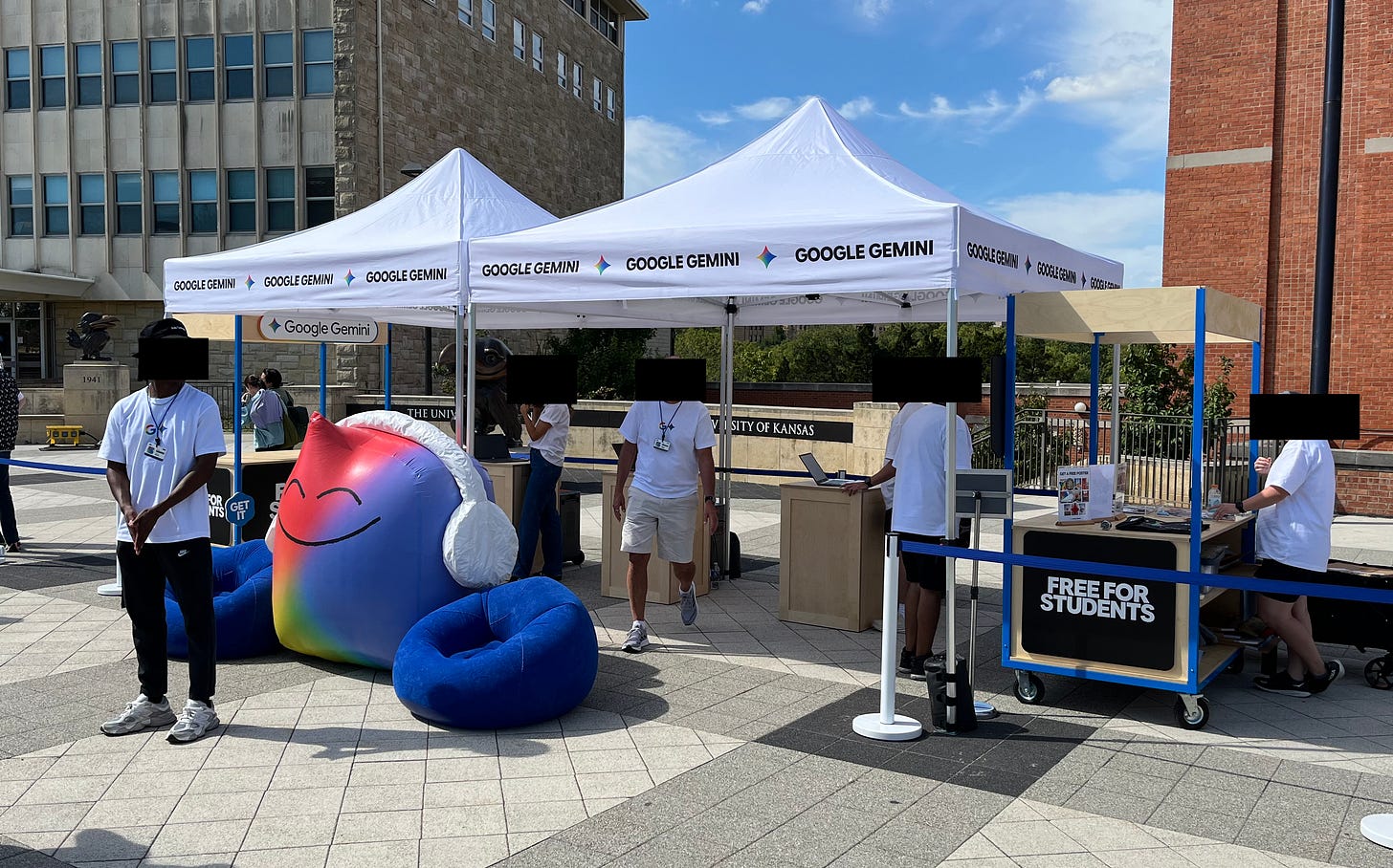 Student workers (faces blocked for privacy/anonymity) staffing a Google Gemini tent outside of the Kansas Union at KU. Sign says “free for students.”