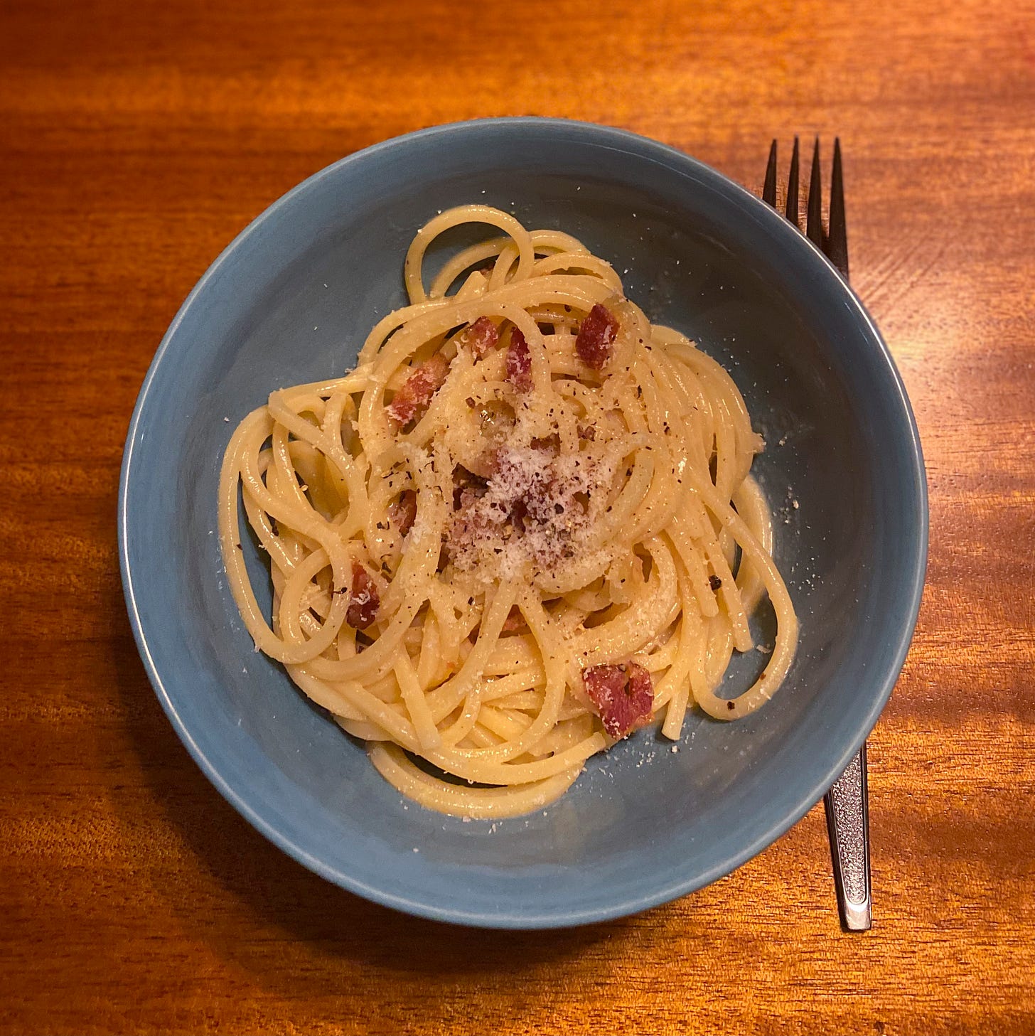 A blue bowl of spaghetti carbonara with grated pecorino and ground pepper on top. A blue bowl of spaghetti carbonara with grated pecorino and ground pepper on top.