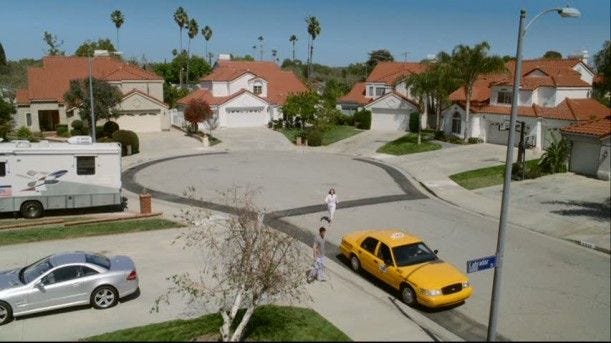 This may contain: a yellow car parked on the side of a road next to a street light and houses