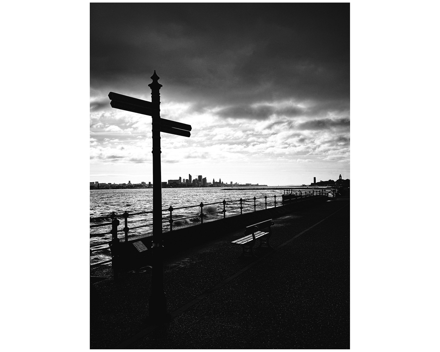 Clouds move over the River Mersey as the tide rolls in. A street sign is silhouetted against the sky.