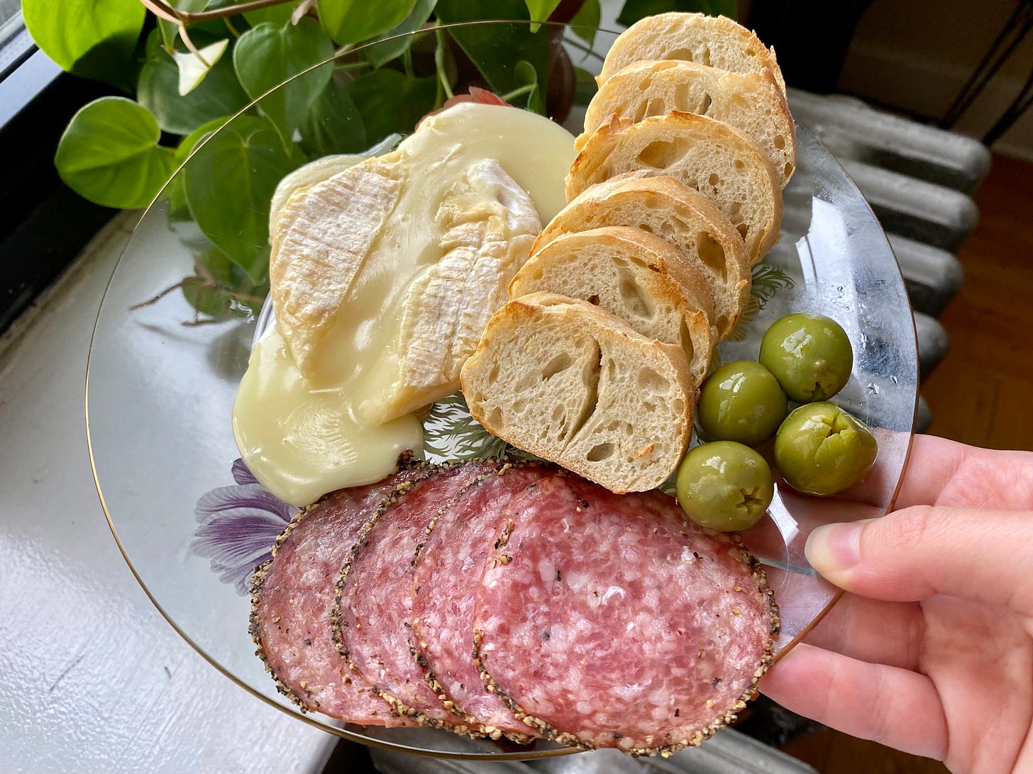 Langherino cheese wheel melted on a plate with toasted baguette slices, green castelvetrano olives, and slices of peppered salami