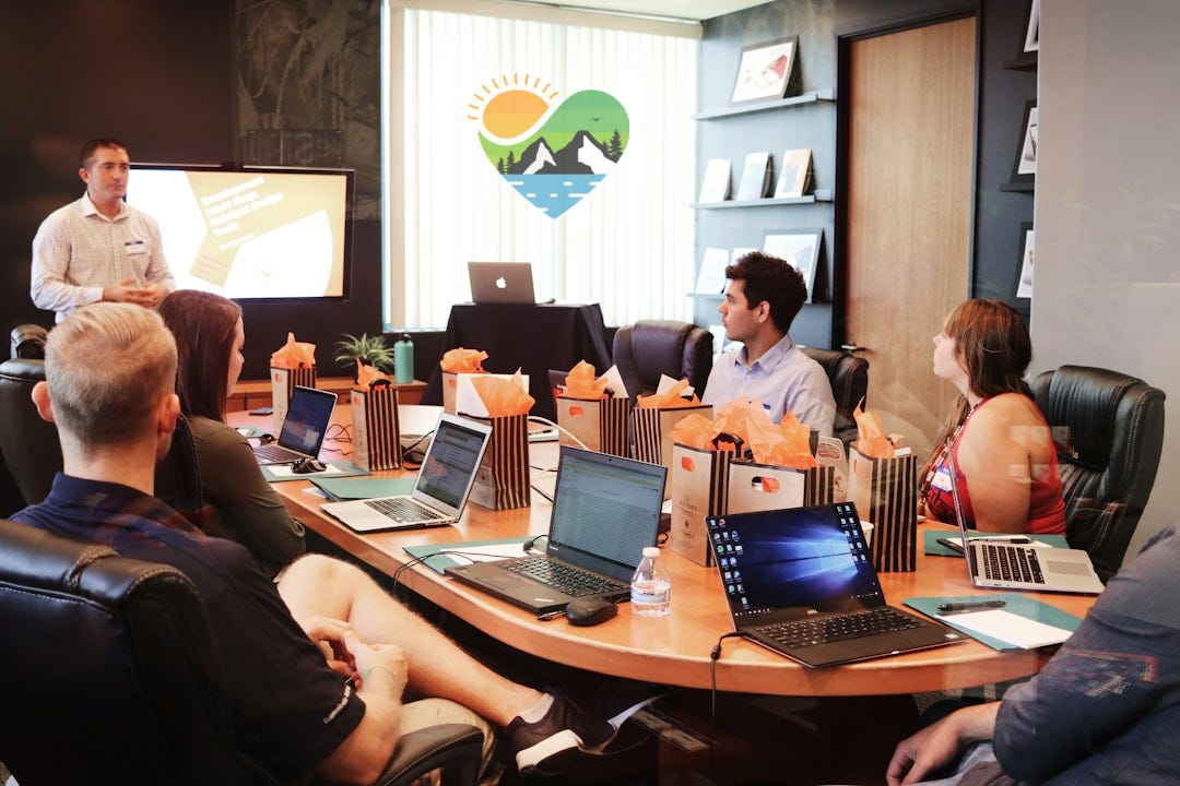 man standing in front of people sitting beside table with laptop computers man standing in front of people sitting beside table with laptop computers