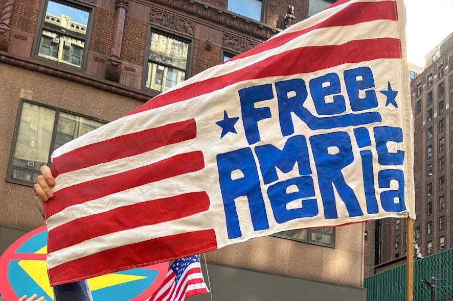 Free America Walkout flag with ‘Free America’ in blue letters waving at a city protest, January 20, 2026.