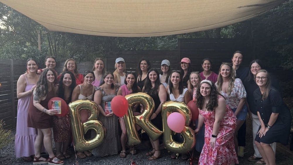 A large group of women at a Beach Reads and Bubbly book club meetup holding gold foil balloons that spell BRB.