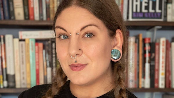 Labor and heavy metal journalist Kim Kelly stands in front of a bookcase
