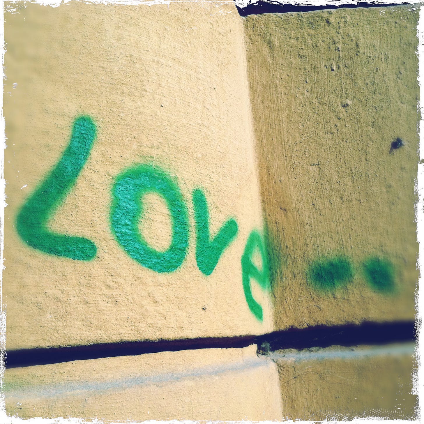 Green spray paint on yellow stone wall reading Love