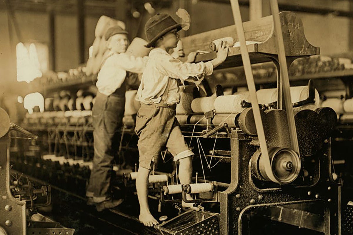 This historical photograph, taken by Lewis Hine in January 1909, depicts young barefoot boys working atop a spinning frame at Bibb Mill No. 1 in Macon, Georgia. Children with small frames were often hired to mend broken threads and replace bobbins.