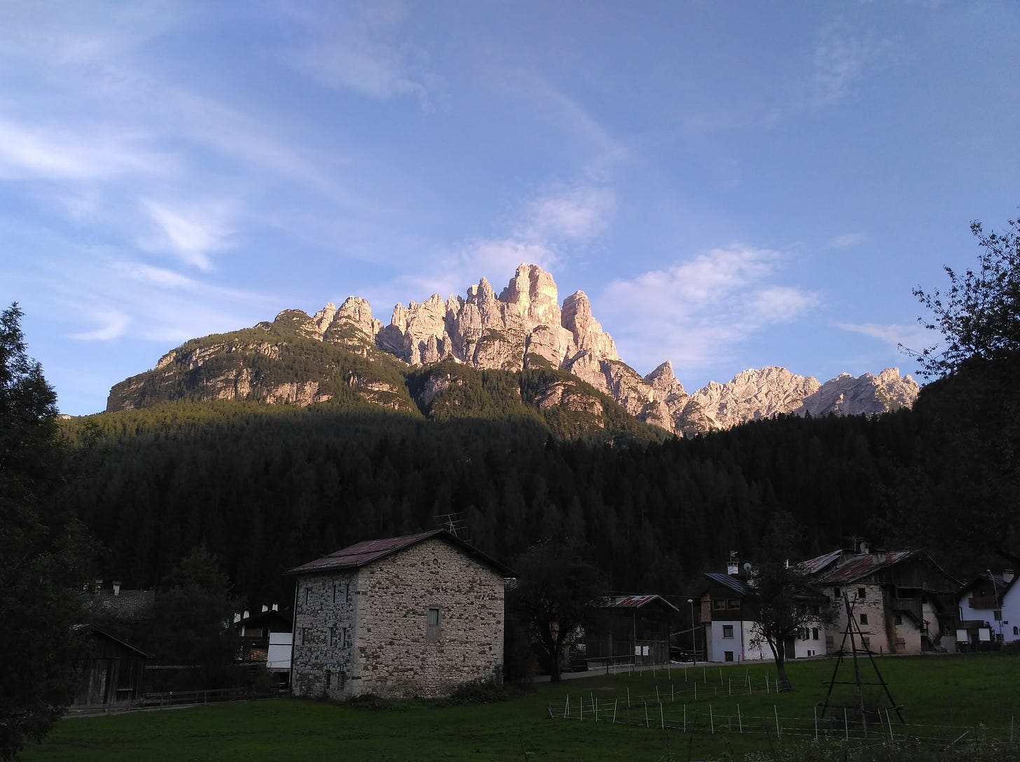 Una casa di pietra in fondo a un prato buio. Sullo sfondo, una montagna illuminata. Una casa di pietra in fondo a un prato buio. Sullo sfondo, una montagna illuminata.
