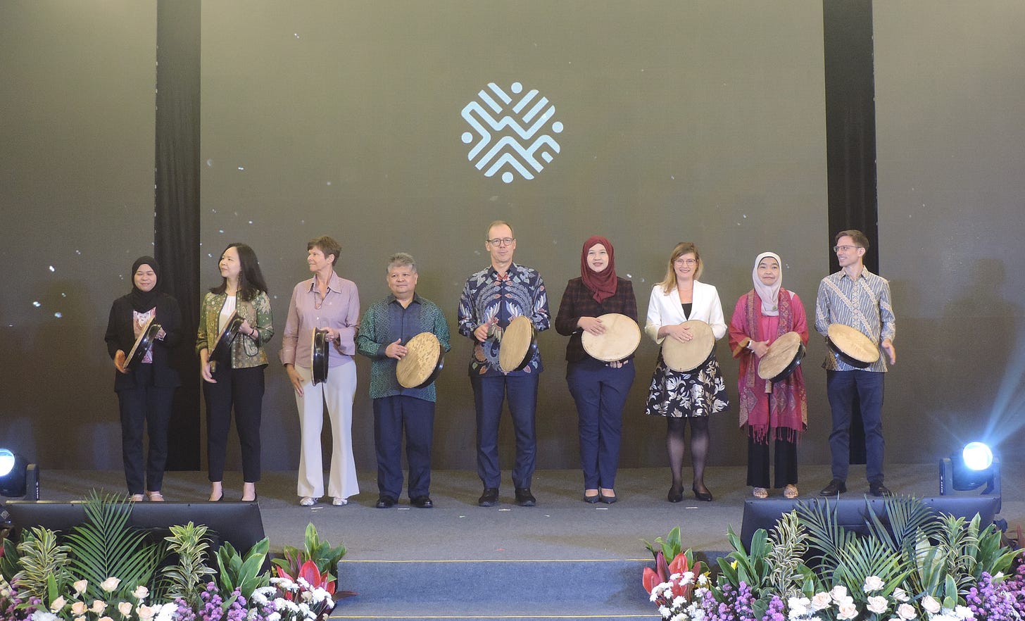 A group of nine people are standing in a row on a decorated stage, each holding a traditional frame drum A group of nine people are standing in a row on a decorated stage, each holding a traditional frame drum