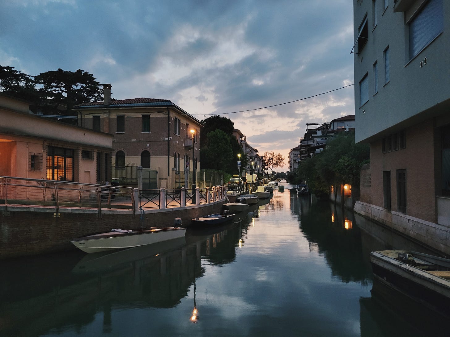 A quiet canal lined with buildings, cars, and boats on Lido at dusk A quiet canal lined with buildings, cars, and boats on Lido at dusk