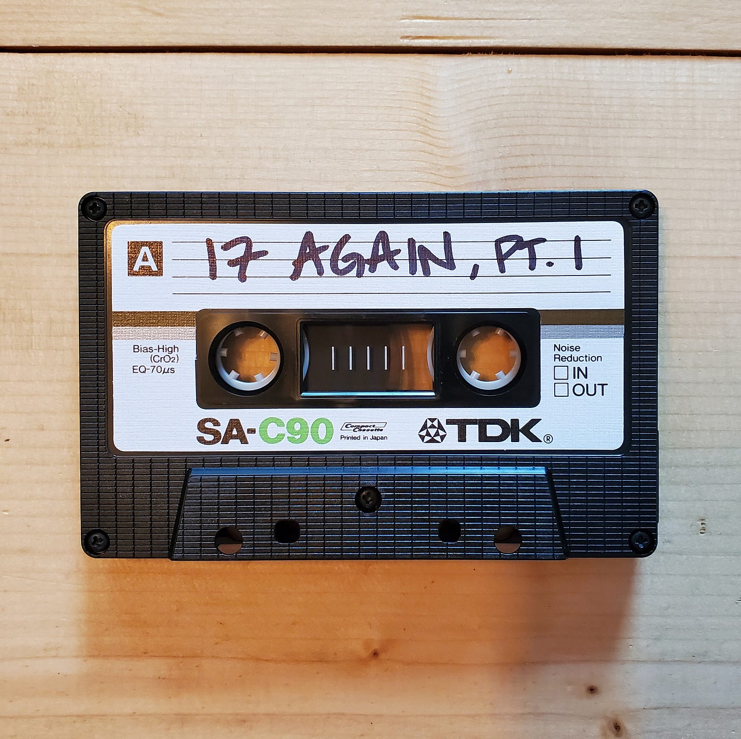 A cassette tape sits on a wooden table. It is labeled "17 Again, Pt. 1" in Sharpie.
