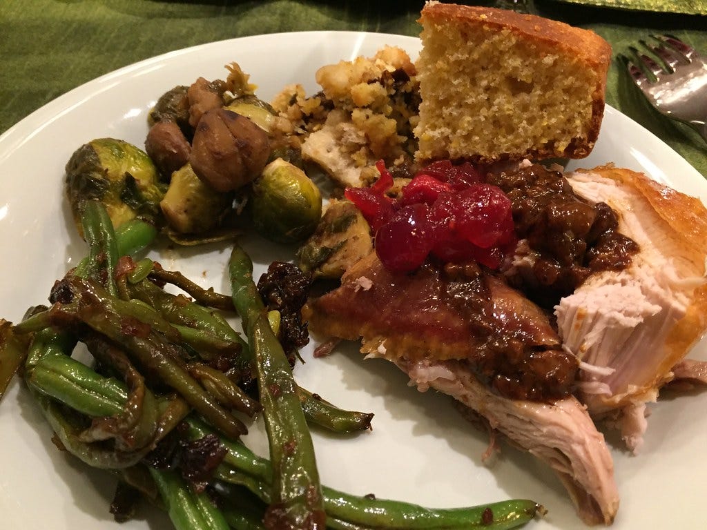Photo of Thanksgiving dinner on a plate including slices of turkey, cranberry sauce, stuffing, green beans and Brussel sprouts
