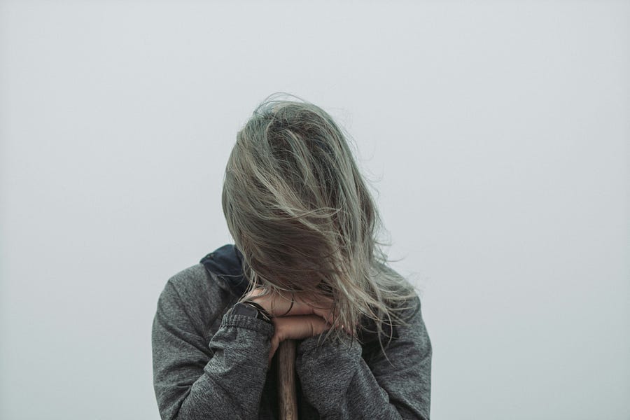 Woman with head down leaning on the end of an oar. Wearing a longsleeved grey shift and background is a foggy background