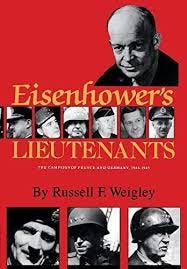 A headshot photo of General Eisenhower dominates the upper portion of the book’s red cover with the title in gold script lettering – “Eisenhower’s” is centered with “Lieutenants” below, centered. Between the words is a mosaic of headshots of six military leaders.  At the bottom of the page are three, slightly larger headshots of three additional leaders – collectively presenting the impression that these are Eisenhower’s Lieutenants.  The Author’s name, in black font rests just above the three images. 