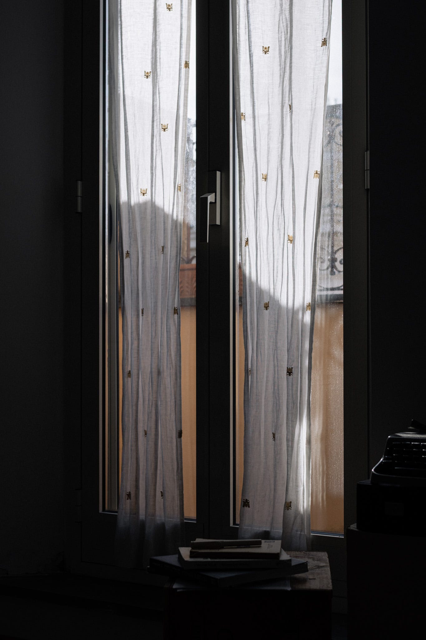 Sheer white curtains hanging in front of a sunlit window, casting gentle shadows inside a quiet room.