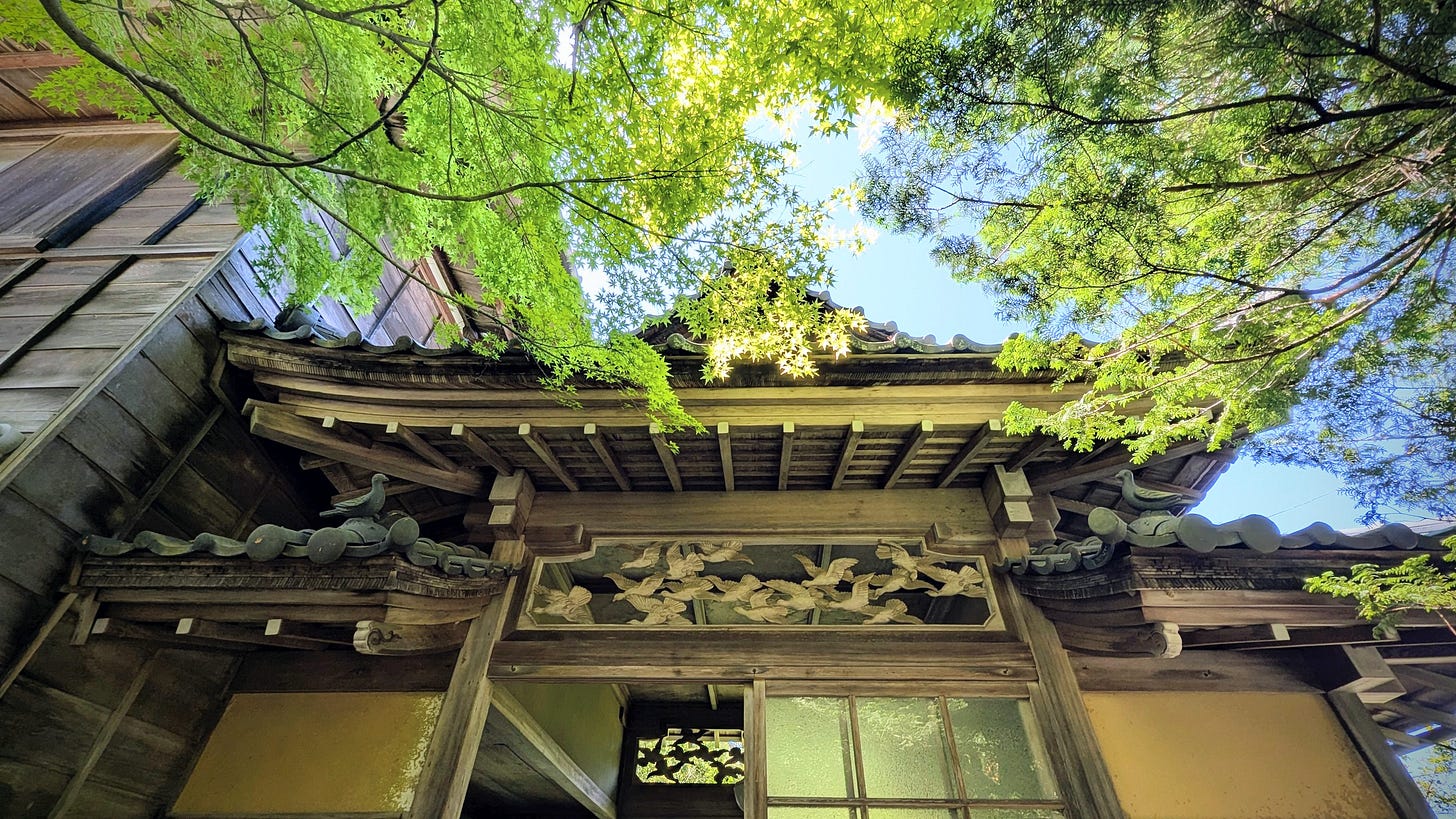 Ornate wooden entrance to an historic Japanese villa surrounded by green tree branches.