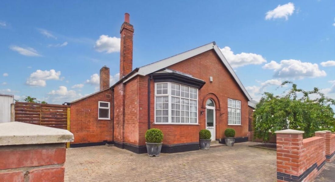 A large brick bungalow with a brick fence in front of it and a blue sky above it