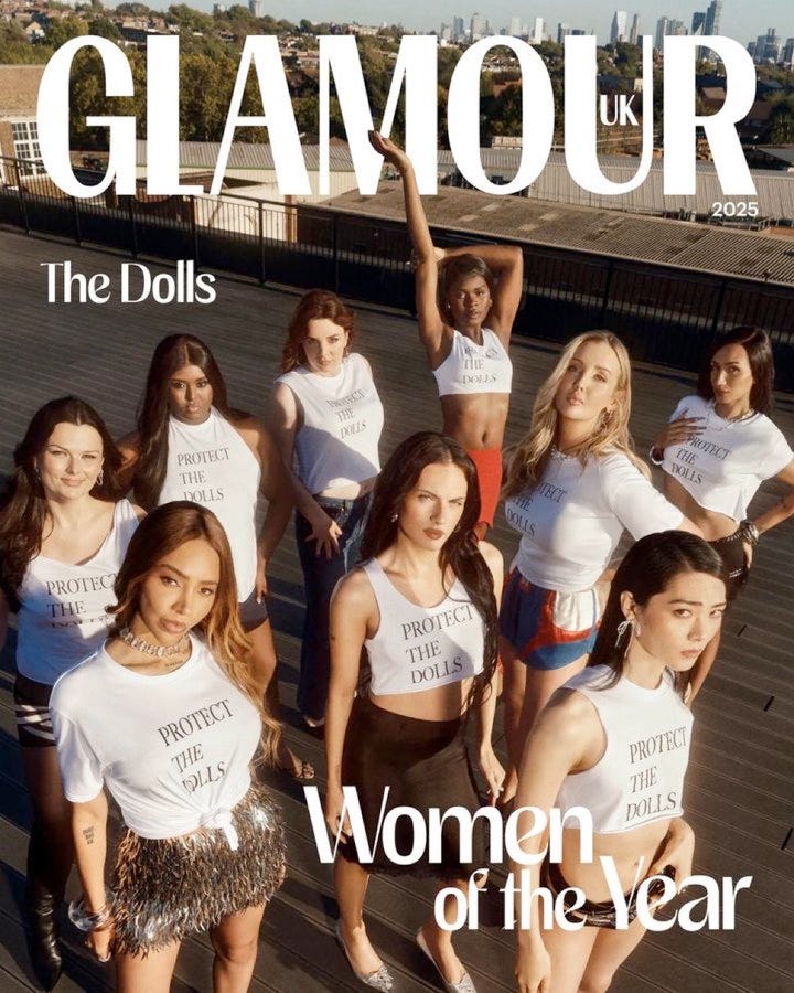 Magazine cover shows diverse group of women on rooftop balcony with city skyline. They wear white tank tops and shorts printed with Protect the Dolls. Poses include standing arms raised and grouped confidently. Title The Dolls at top with Glamour UK logo. Bottom text Women of the Year and 2025 designation.