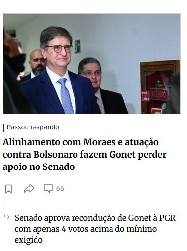 Three men in suits stand together in a formal indoor setting with a red cabinet behind them one central man with glasses smiles slightly while the others look on professionally the scene appears to be a political or official gathering.