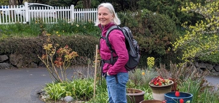 A woman in jeans, jacket, and backpack, smiling at the camera