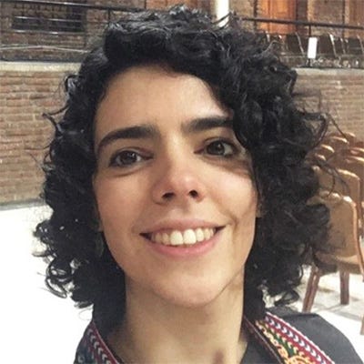 Mulher branca, cabelos negros encaracolados à altura do pescoço e sorridente