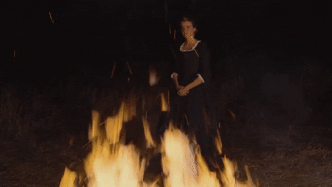 Héloïse from "Portrait of a Lady on Fire" stands in the dark walking behind open flame.