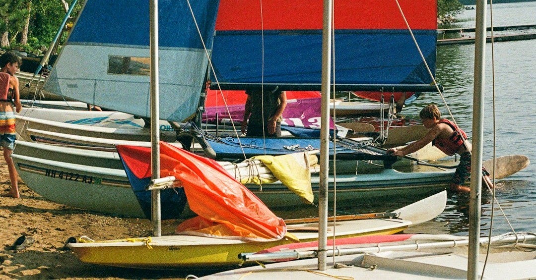 Colorful sailboat sits on a lake shore.