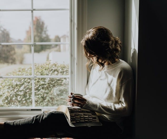 A woman sitting on a window sill reading a book