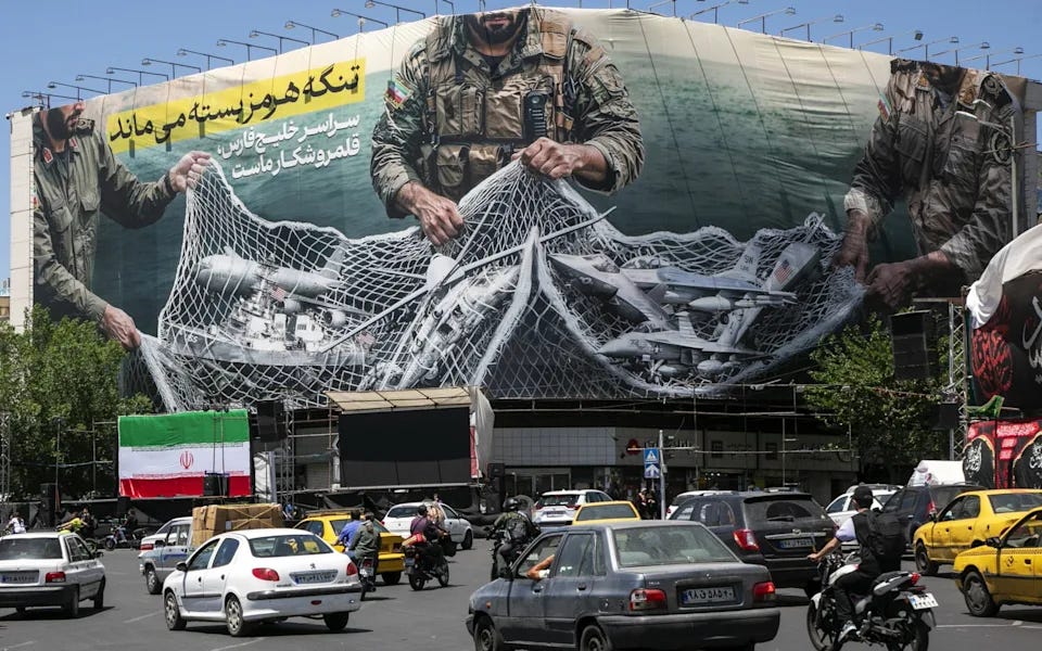 A poster depicts Iranian soldiers holding a net in the shape of the Strait of Hormuz, with US military aircraft ensnared in a fishing net