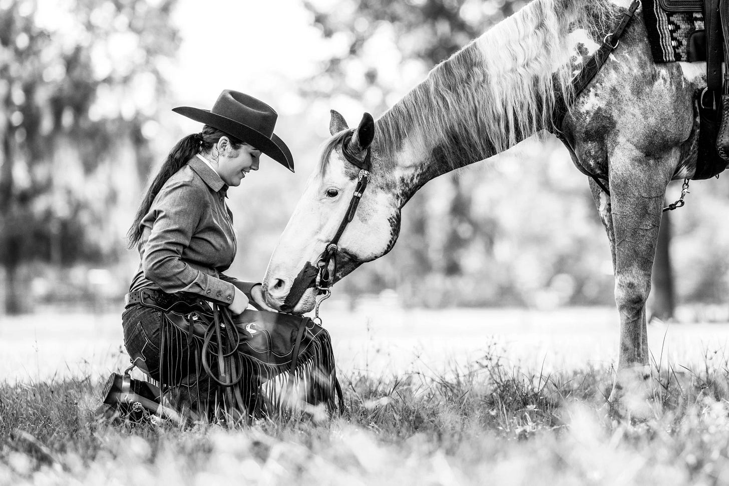 a black and white photo of a cowgirl kneeling before her horse in full tack to feed him - nostalgic a black and white photo of a cowgirl kneeling before her horse in full tack to feed him - nostalgic