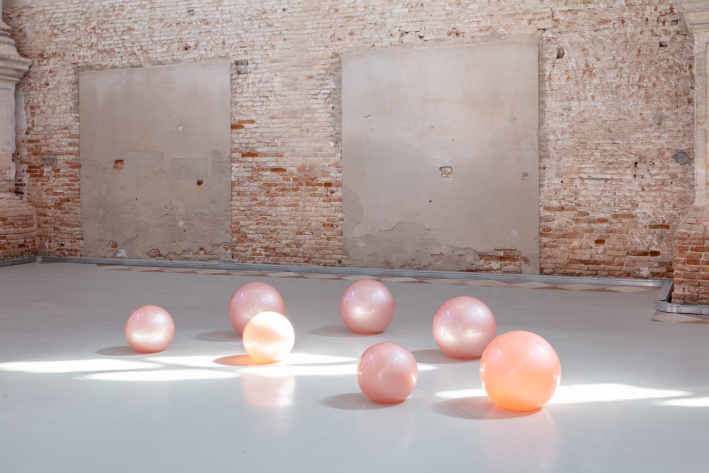 Set against a brick wall, pink and orange translucent glass balls lie on the floor. Set against a brick wall, pink and orange translucent glass balls lie on the floor.