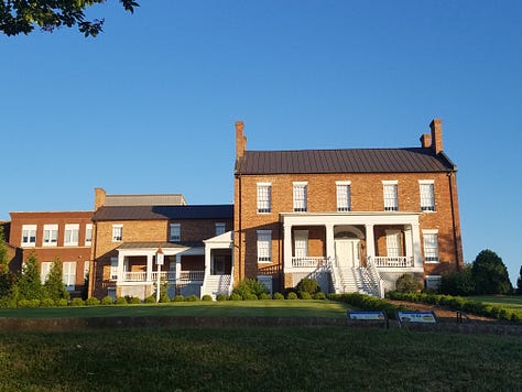 The Dickson Williams Mansion, a brick building with a white porch; the parlor, showing a round table surrounded by black chairs on a red oriental rug in front of a fireplace; the kitchen area, showing original north carolina furniture; bedrooms of the house, along with a portrait of General John Hunt Morgan sitting in a chair in a black coat with tall black boots; and the bed where he spent his last night.