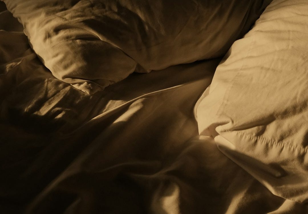 An unmade bed in a dark room An unmade bed in a dark room