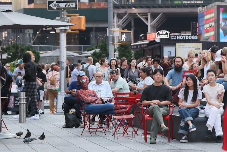 A man dressed in a Spider-Man costume sits among a crowd of onlookers.