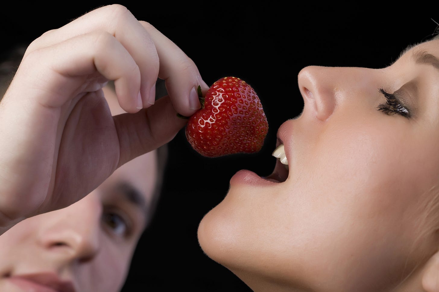Man background, giving strawberry to woman, foreground