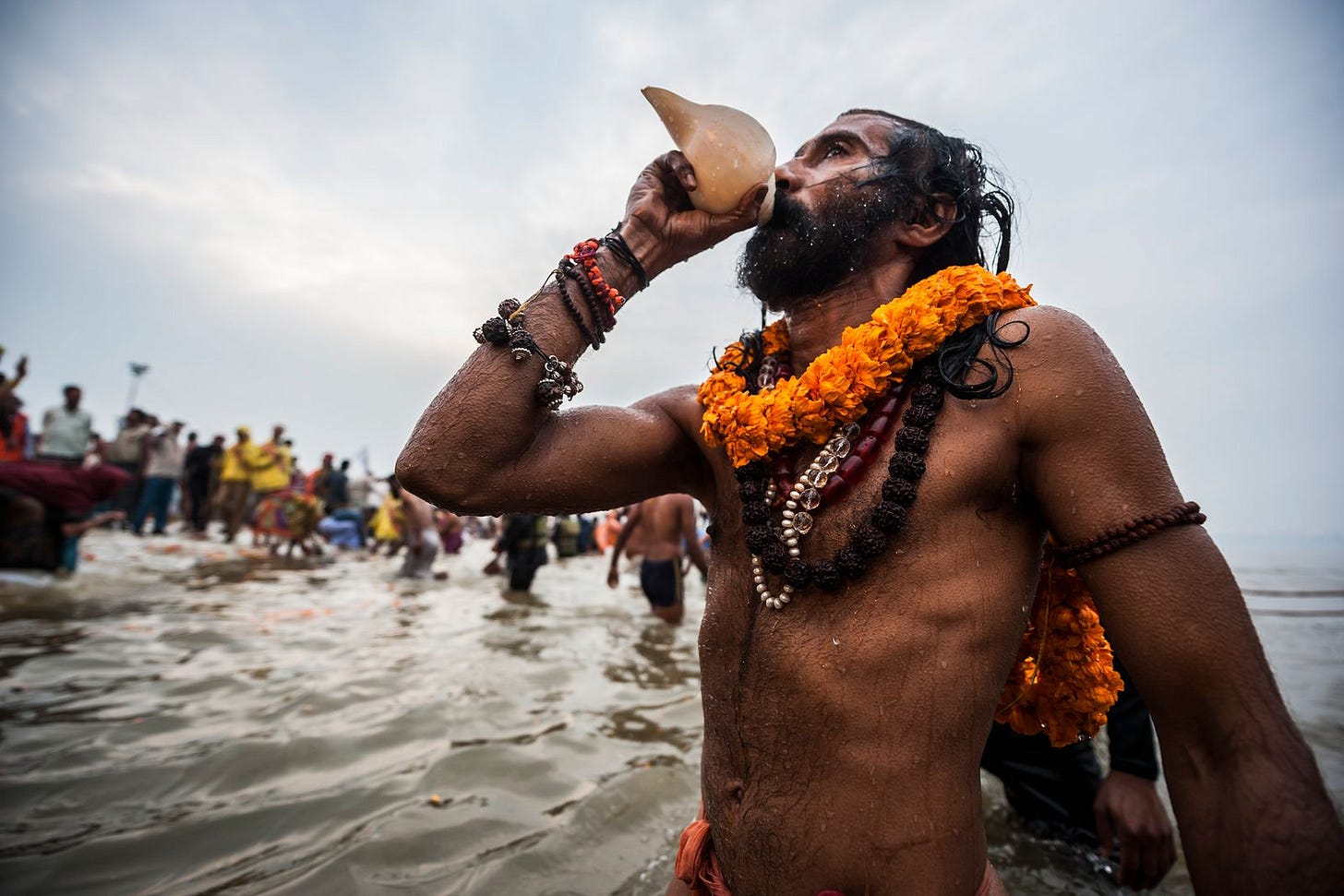A Naga sadhu blows a conch shell while bathing in the Ganges