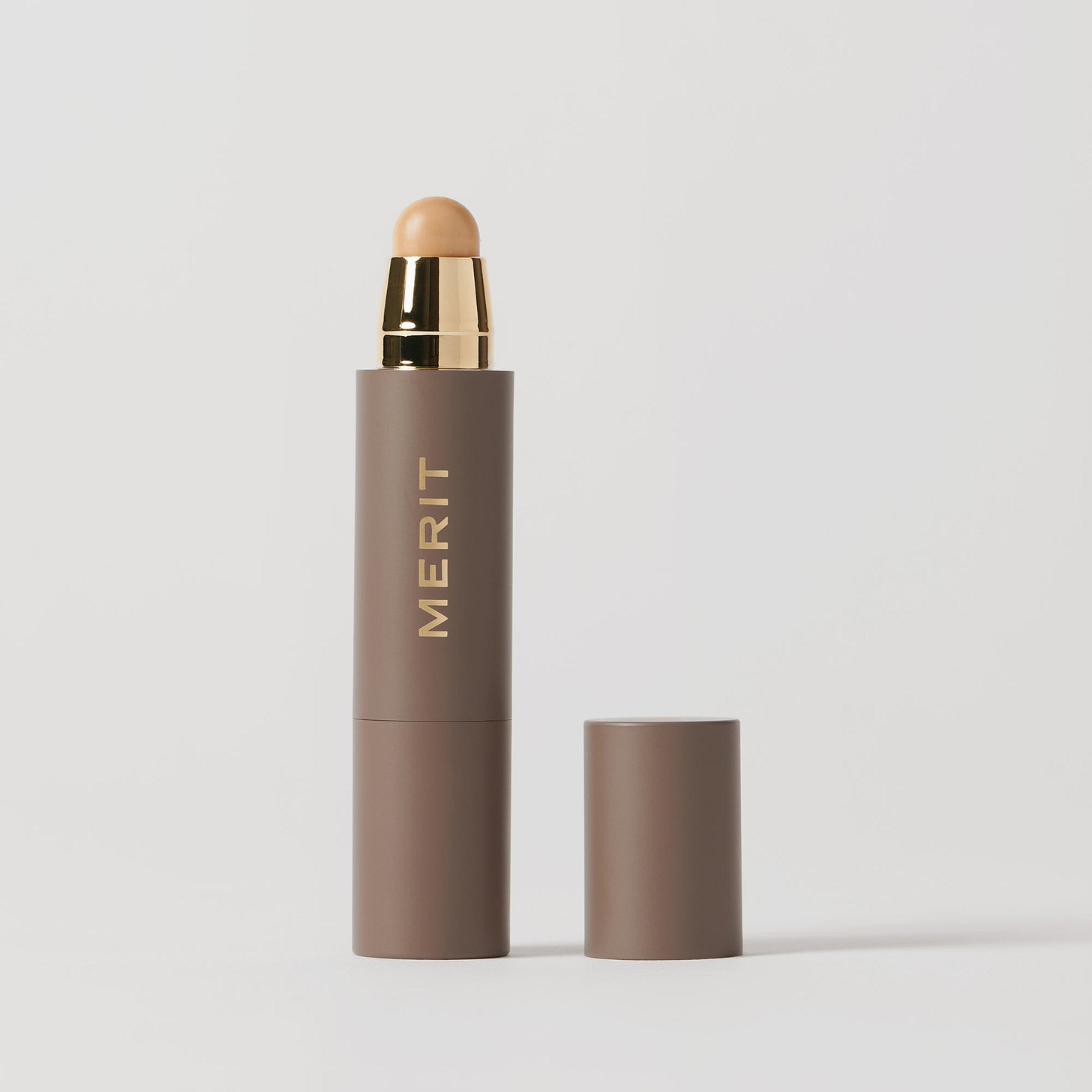 Master || A stick complexion product with MERIT written on it, with the cap removed, showing the product in shade Linen.